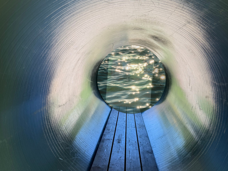Schauend durch einen Tunnel ist eine Wasseroberfläche in der Sonne glitzernd zu sehen